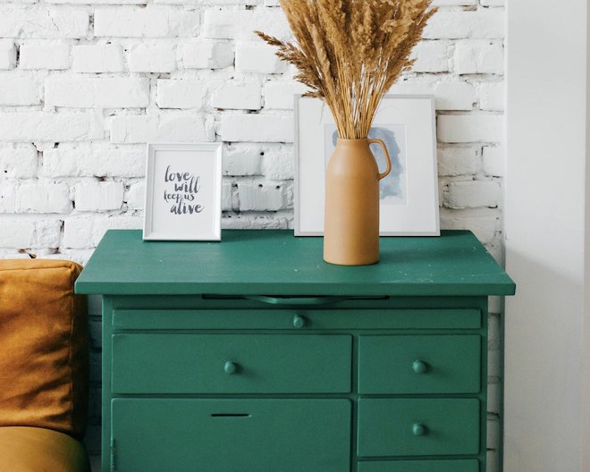 A green drawer with two portraits and one vase on the top of it.